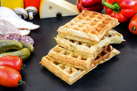 Traditional belgian waffles with cheese and vegetables on a black background. Cucumber. Ham. Mushrooms. Tomato. Salami. Cheese. Pepper. Copy spaceの写真素材