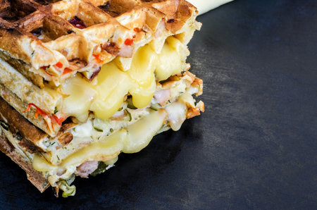 Traditional belgian waffles with cheese and vegetables on a black background. Ham. Mushrooms. Tomato. Cheese. Pepper. Copy space. Closeupの写真素材
