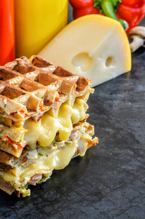 Traditional belgian waffles with cheese and vegetables on a black background. Ham. Mushrooms. Tomato. Cheese. Pepper. Copy space. Closeupの写真素材