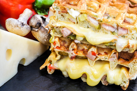 Traditional belgian waffles with cheese and vegetables on a black background. Ham. Mushrooms. Tomato. Cheese. Pepper. Closeupの写真素材
