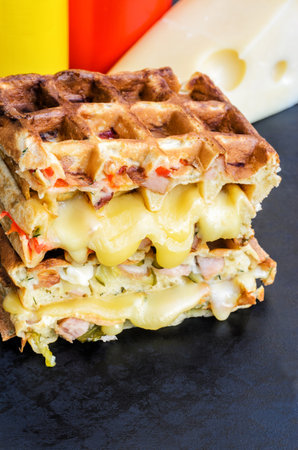 Traditional belgian waffles with cheese and vegetables on a black background. Ham. Mushrooms. Tomato. Cheese. Pepper. Copy space. Closeupの写真素材