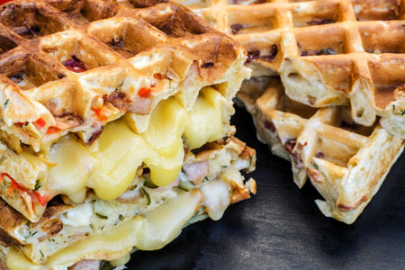 Traditional belgian waffles with cheese and vegetables on a black background. Ham. Mushrooms. Tomato. Cheese. Pepper. Copy space. Closeupの写真素材