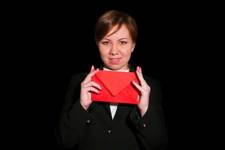Pretty young business woman smiles and holds blank envelope isolated on blackの写真素材
