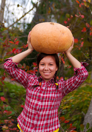 Girl holding up a large pumpkin in the gardenの写真素材