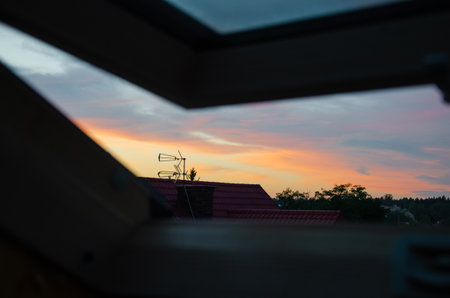 Beautiful sunset sky view through open attic window in country house