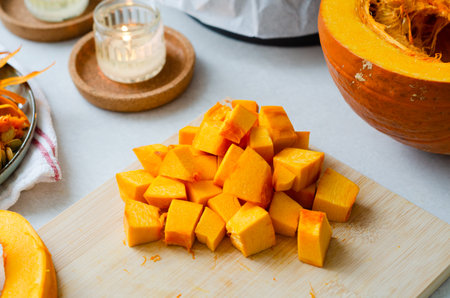 Close up of bright orange cut pumpkin cubes on wooden cutting board for autumn recipesの写真素材
