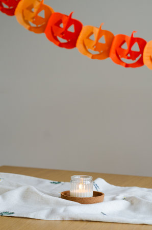 Minimal halloween decor with candle in glass on stand and paper garland in backgroundの写真素材