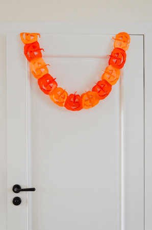 Paper pumpkin garland hanging on white door for Halloween party decor with copy spaceの写真素材