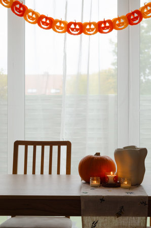 Minimal autumn table decor with pumpkin, white vase and candles by window with paper pumpkin garland for Halloweenの写真素材
