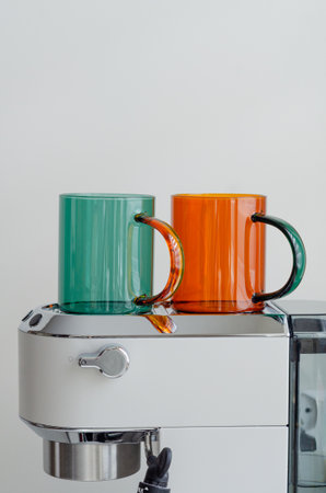 Cozy morning with green and orange glass cups warming on white portafilter coffee machine for home coffee preparationの写真素材