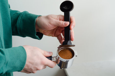 Cozy morning with mans hands tamping ground coffee in portafilter for home espresso preparationの写真素材