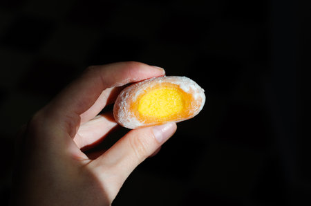 Close-up of woman holding bitten frozen yellow mochi ice cream with mango fillingの写真素材