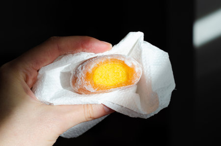 Close-up of woman holding bitten frozen yellow mochi ice cream with mango filling