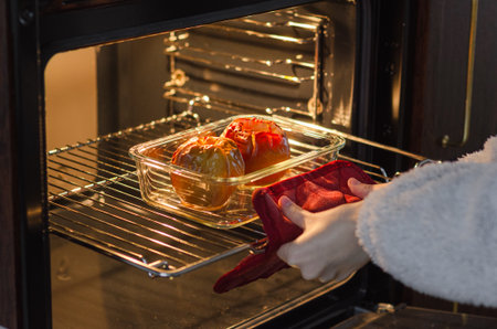 Woman taking golden baked farm apples from oven with red mitt, healthy sugar-free dessert or snackの写真素材