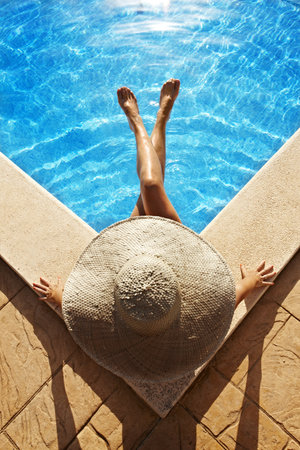Woman with hat sitting at poolsideの写真素材