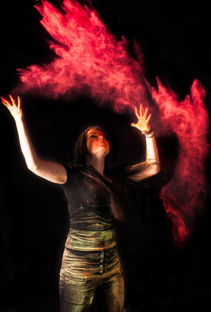 Beautiful young woman Holi paint fest with colorful powder covering her face and a cloud of dust. On black with rainbow bursts of color. High quality photoの写真素材