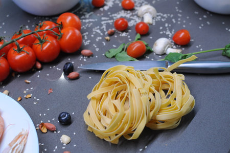 Spaghetti and fettuccine with ingredients for cooking pasta on wooden table with blank of round wooden kitchen board, top view. Rustic style. Flat lay. High quality photoの写真素材