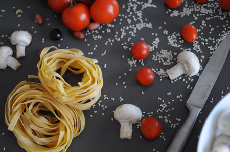 Spaghetti and fettuccine with ingredients for cooking pasta on wooden table with blank of round wooden kitchen boardの写真素材