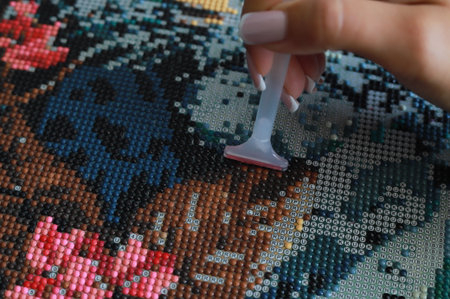 Girl collect diamond painting. Diamond embroidery with a tweezers. Acrylic rhinestones.