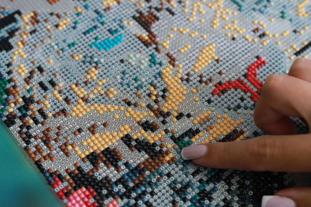 Girl collect diamond painting. Diamond embroidery with a tweezers. Acrylic rhinestones. Close-up, selective focus.の写真素材