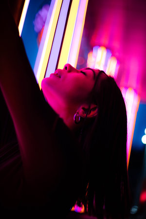 Glamour in neon illumination. Striking portrait of woman wearing stylish sunglasses that reflect...