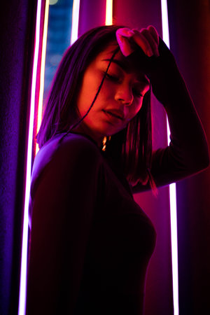 Glamour in neon illumination. Striking portrait of woman wearing stylish sunglasses that reflect vibrant neon lights in background. High quality photoの写真素材