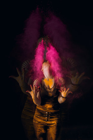 Beautiful young woman Holi paint fest with colorful powder covering her face and a cloud of dust. On black with rainbow bursts of color. High quality photoの写真素材