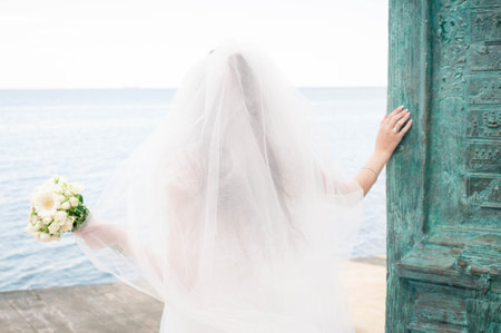 Bride on the coast of the sea. On the bride is a long wedding dress with lace and an open back.の写真素材