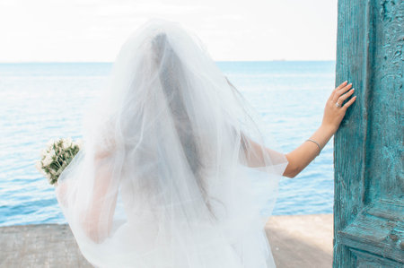 Bride on the coast of the sea. On the bride is a long wedding dress with lace and an open back.の写真素材