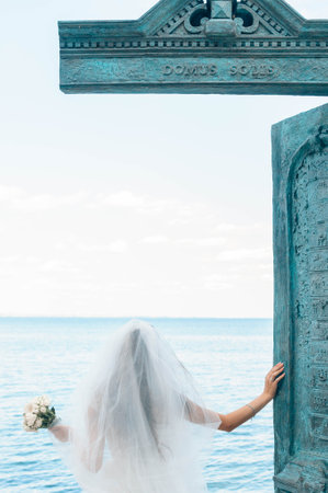 Bride on the coast of the sea. On the bride is a long wedding dress with lace and an open back.の写真素材