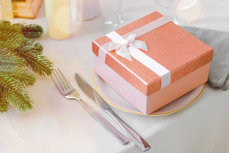 Festive table setting with a pink gift box in a plate on the table. Banner. Side view, garland light. Christmas or New Year concept. High quality photoの写真素材