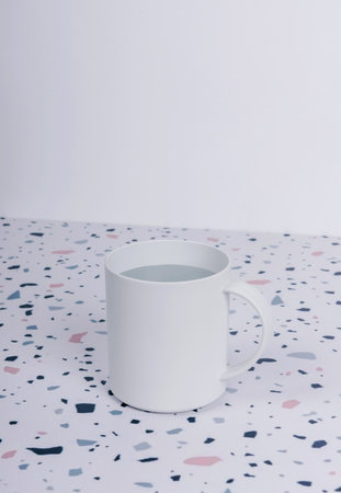 A closeup shot of a ceramic white mug with water staying on the table.