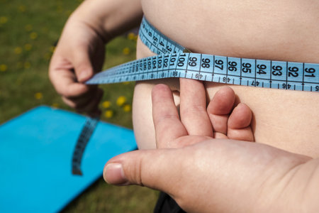 fat woman in black sweater measures waist circumference with centimeter tape, belly stands, concept time to lose weight, wrong lifestyle, consequences of inactivity, unhealthy diet. outdoorの写真素材