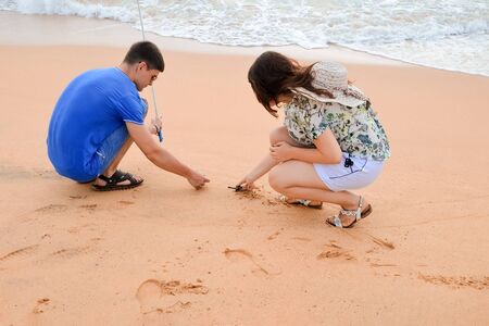 Brunette guy with camera and brunette girl in white shorts walking beach. Happy young couple holding turtles in hands, volunteers save and release turtles into ocean. Sea Conservation Research Center.の写真素材