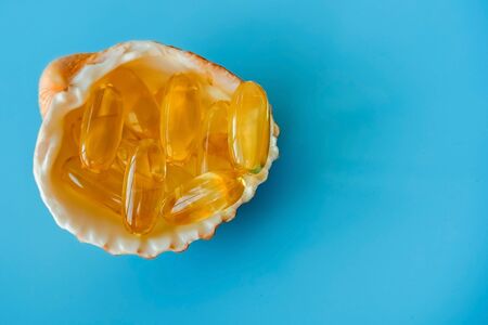 Omega 3 and vitamin D capsules on shell, fish oil pills.
