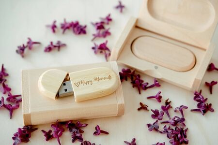 Wooden brown usb flash drives with boxes with the text Happy Moments with lilac petals on a white...