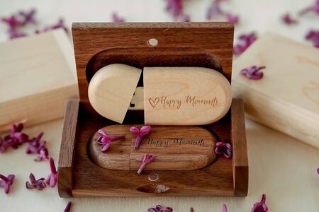 Wooden brown usb flash drives with boxes with the text Happy Moments with lilac petals on a white...