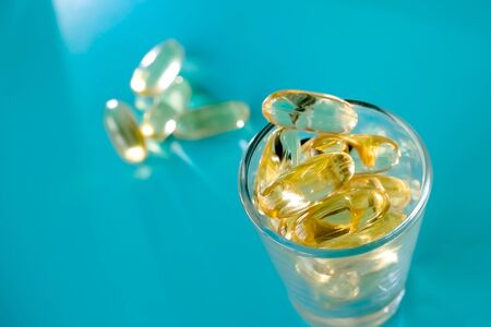 A handful of omega 3 capsules with a glass beaker on a blue backgroundの写真素材