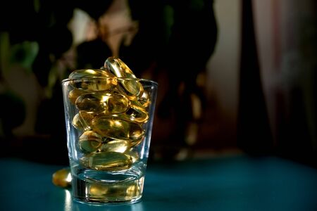 A glass cup with omega 3 vitamins stands on a blue table near the window, near a birch tree,