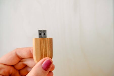 Female hand holds a stylish wooden flash drive on a light background. beautiful photo feedback to...