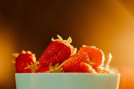 red juicy ripe strawberries in a blue vase on a black background. Sun warm rays, back light, horizontal 
の写真素材