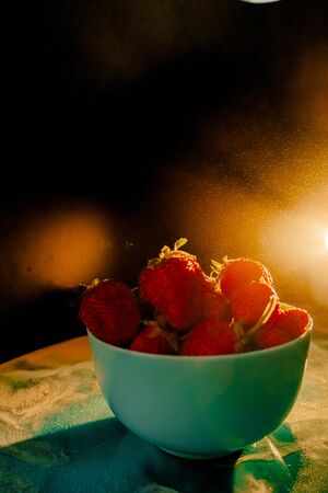 red juicy ripe strawberries in a blue vase on a black background. Drops of water, warm sunshine, back light, verticalの写真素材