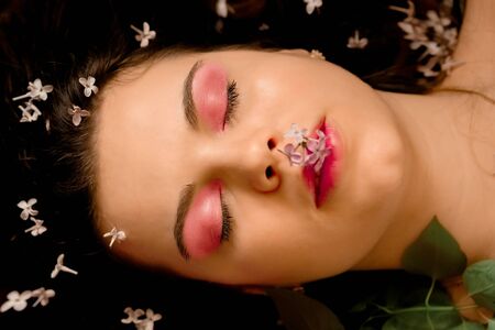 Portrait of a beautiful girl with bright makeup on her eyes and lips. Bouquet lilac around the face, spring girl, flowers in her hairの写真素材