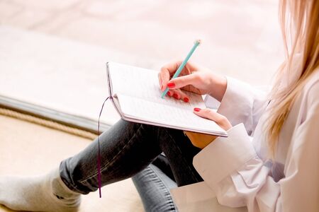 Beautiful sexy girl sits on a windowsill with a notebook and thinks. Details close up. A lonely woman in a man's shirt reads a book, keeps notes in a notebookの写真素材
