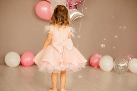 little girl in a bright room in a smart pink dress. balloons lie on the floor, concept of childhood, birthdayの写真素材