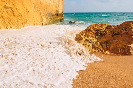 Waves crash on rocks on the sandy shores of benagil beach in portugalの写真素材