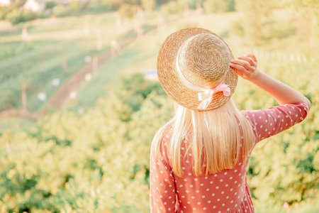 portrait of a beautiful young blonde girl. girl on a picnic in a spring park, looking into the distance, view from the back to a meadow with grassの写真素材