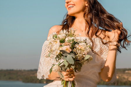 beautiful slender girl with long curly hair in a lace dress. woman holding a bouquet of flowers and laughing against the skyの写真素材