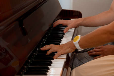 female and male hands, a girl with a guy playing the piano, fingers close-up, horizontal imageの写真素材