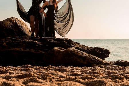 photo session at dawn by the sea, two girls with a tulle skirt are dancing on the rocks, horizontal imageの写真素材